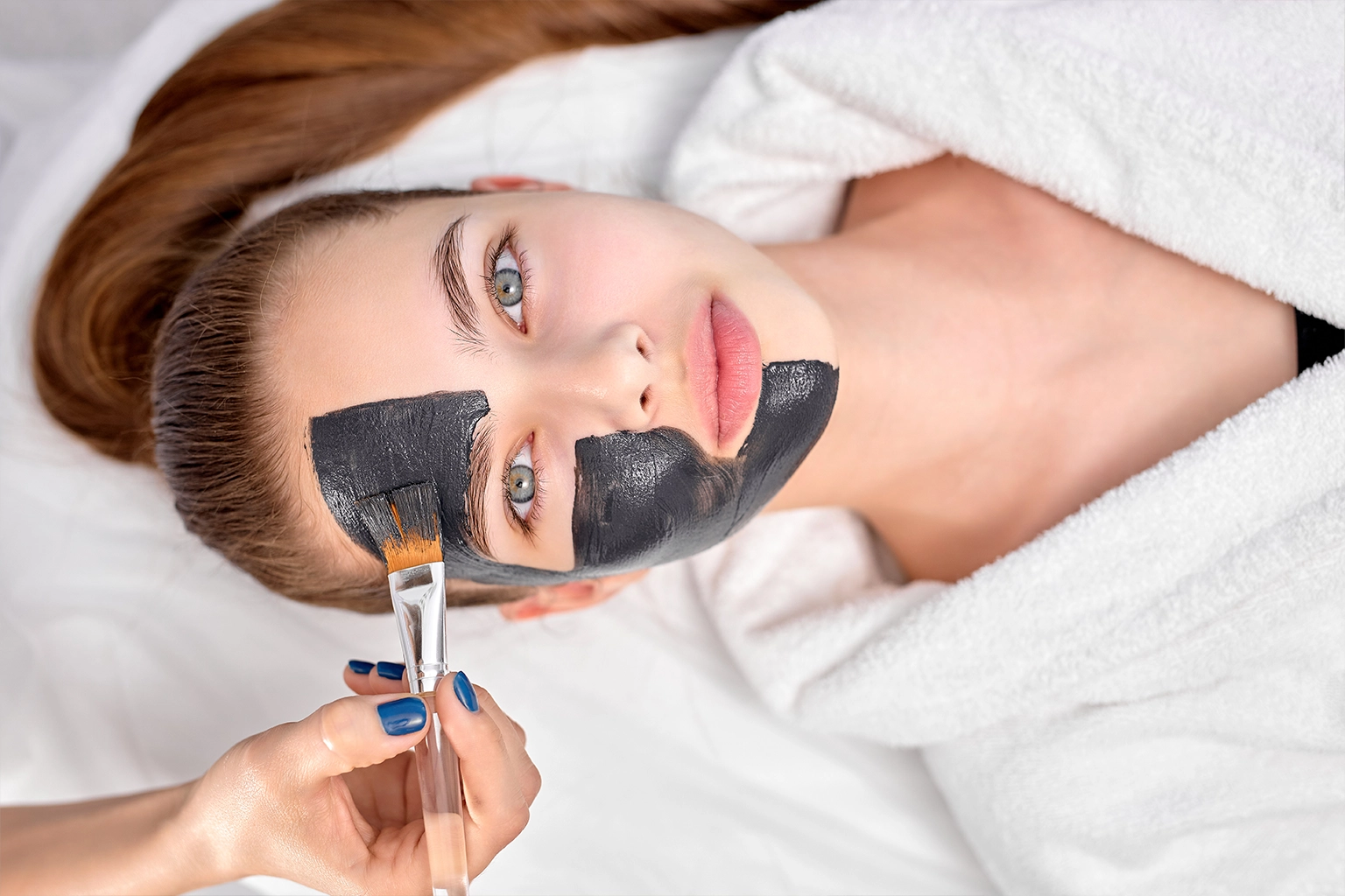 Aesthetician applying carbon mask on woman's face during carbon peel treatment, enhancing skin texture and reducing imperfections